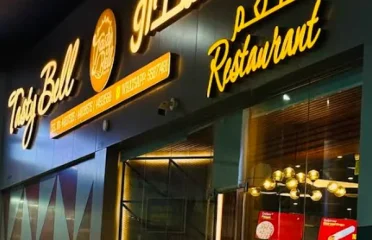 Restaurant storefront signage with illuminated Arabic and English lettering at Tasty Bell restaurant during nighttime.